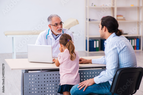 Small girl with her father visiting old male doctor