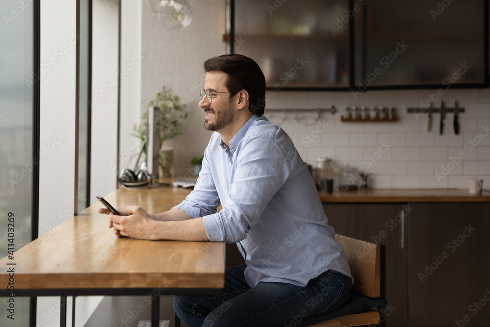 Dreamful millennial guy look at picture window after reading positive news on cell screen refresh pleasant event in memory. Young man get message from beloved woman feel happy imagine romantic date Dreamful millennial guy look at picture window after reading positive news on cell screen refresh pleasant event in memory. Young man get message from beloved woman feel happy imagine romantic date
