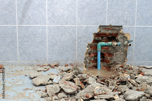 Plumbing problems. A wall of a bathroom is opened to find a leak from a pipe leaving rubble on the floor.