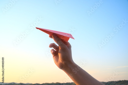 Hand holding a pink paper airplane on sunrise sky background