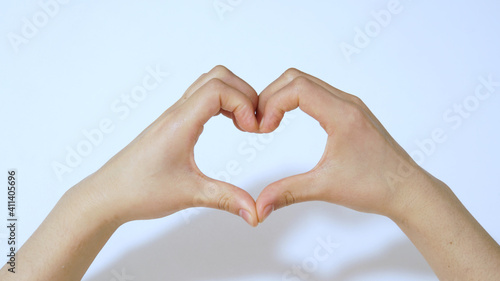 Female hands in the form of heart on white background under light.