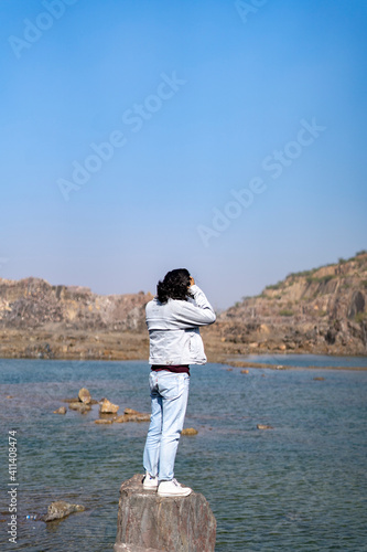 Young indian boy standing on a cliff near a landscape of a lake and mountain in the background.