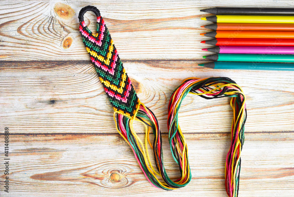 Unfinished woven friendship bracelet with selected palette of crayons colors on wooden table Unfinished woven friendship bracelet with selected palette of crayons colors on wooden table