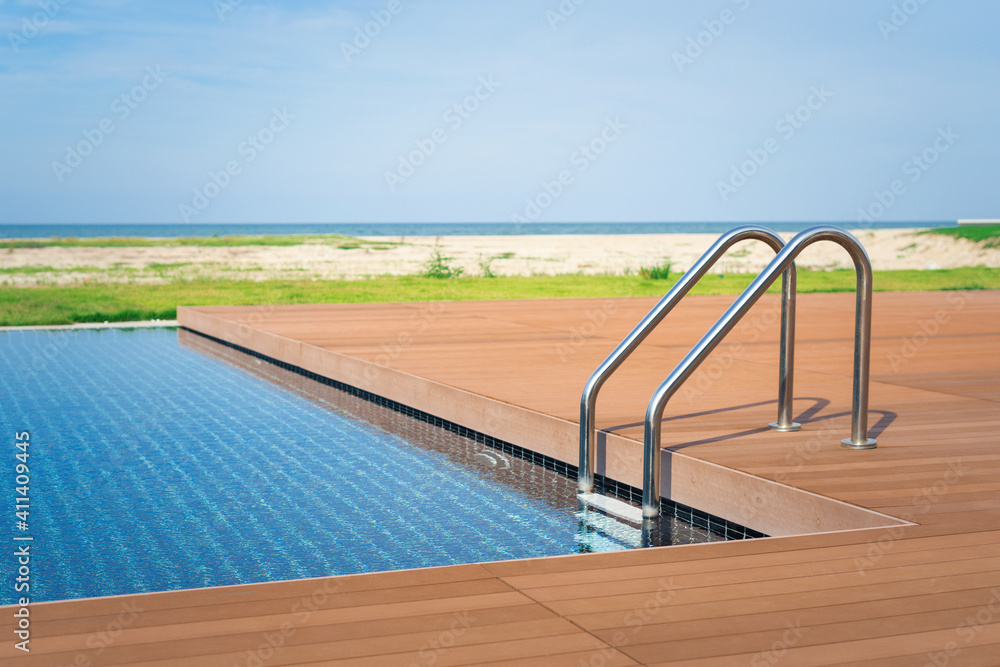 The edge Luxury swimming pool with stair and wooden deck at hotel on the beach.