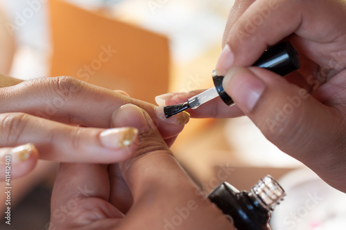 Woman nail paint with a thin brush with top varnish care cosmetics in the salon.