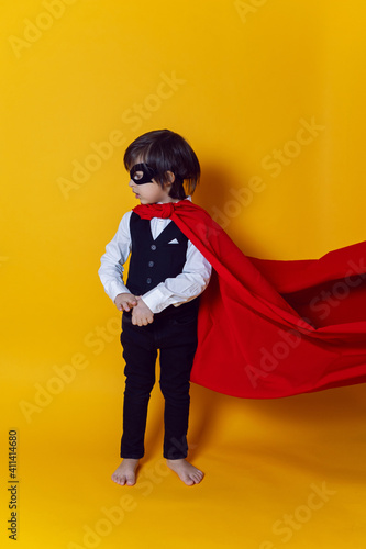 boy child super hero in a suit and black mask in the studio on a yellow background barefoot © saulich84