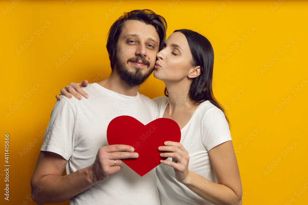 man and a woman in white T-shirts hold a paper heart in the studio on Valentine's Day