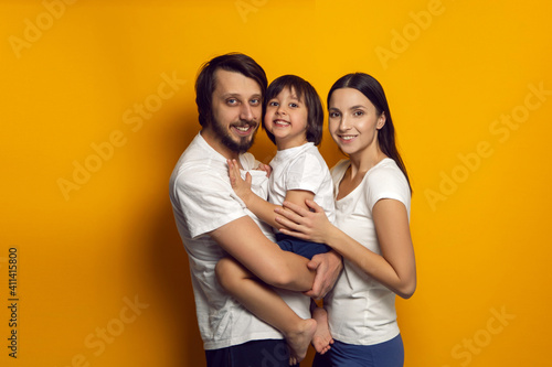 happy family of three a boy and a child in white T shirts stand on a yellow background