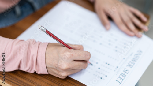 Close up of a young female university student’s hand writing the answer of the examinations on answer sheet in the classroom.