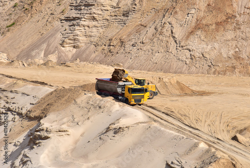 Wheel loader loading sand into dump truck at the opencast mining quarry. Mining truck transports sand in open pit mine. Quarry in which sand and gravel is excavated from the ground. Mining industry photo