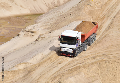 Truck with tipper semi trailer transported sand from the quarry. Dump truck working in open pit mine. Sand and gravel is excavated from ground. Mining industry photo