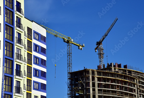 Tower cranes in action on blue sky background. Construction of new multi-storey buildings. Residential building is being constructed use of crane. Pouring of concrete in formwork