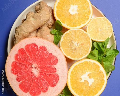 Colorful cirtus slices over blue background. Cut lemons and grapefruit with ginger on a plate. photo