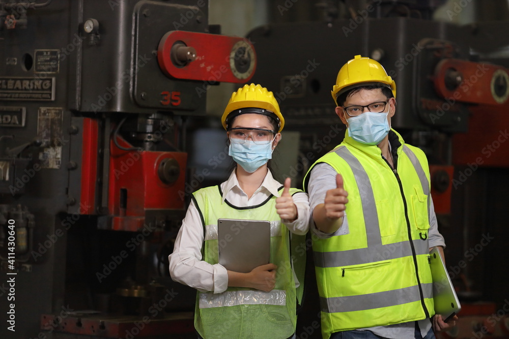 Team of engineer in full safety equipment with facial mask is working and showing thumbs up inside heavy industrial factory for new normal during coronavirus or covid-19 pandemic Team of engineer in full safety equipment with facial mask is working and showing thumbs up inside heavy industrial factory for new normal during coronavirus or covid-19 pandemic