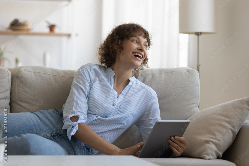 Overjoyed Caucasian female relax on sofa at home have fun suing tablet shopping online. Smiling young woman rest on couch in living room browse surf wireless internet on pad. Technology concept. Overjoyed Caucasian female relax on sofa at home have fun suing tablet shopping online. Smiling young woman rest on couch in living room browse surf wireless internet on pad. Technology concept.
