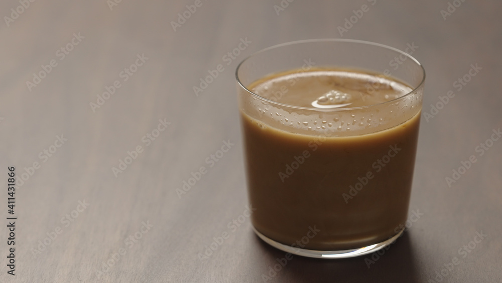 pour cream in coffee in tumbler glass on walnut wood table with copy space pour cream in coffee in tumbler glass on walnut wood table with copy space