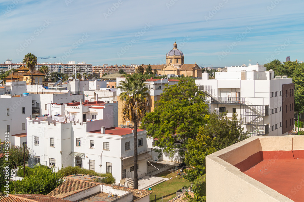 View of the rooftops of Seville on a beautiful sunny morning (Andalusia, Spain). White buildings with red-painted roofs on the horizon. Cityscape overlooking a large church.