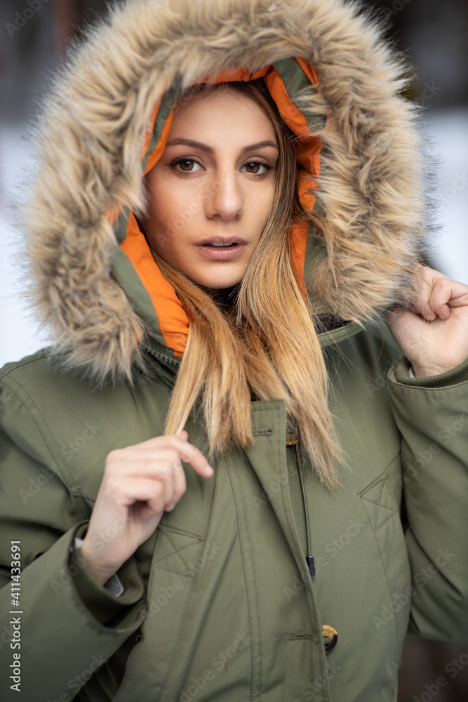 portrait of blonde girl in a green winter coat with a hood with furry fur on the snow in the mountains in winter portrait of blonde girl in a green winter coat with a hood with furry fur on the snow in the mountains in winter