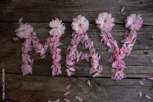 The inscription "May" from pink petals (sakura) on a wooden background. Spring concept.
