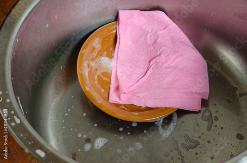 Photos Pink viscose dishcloth and brown plate in the metal kitchen sink with foam