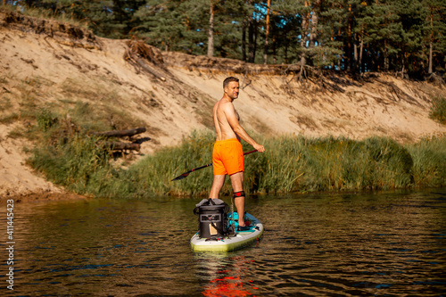 A young athletic man rowing with a SUP stand up paddle board in the river. Back view