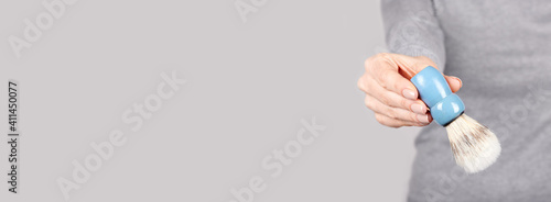 Hand with shaving brush on grey background.