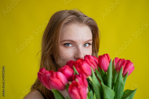 Woman with a bouquet of red tulips on a yellow background. Happy girl in a black dress holds an armful of flowers . Gift for Valentine's Day. The most romantic day of the year.