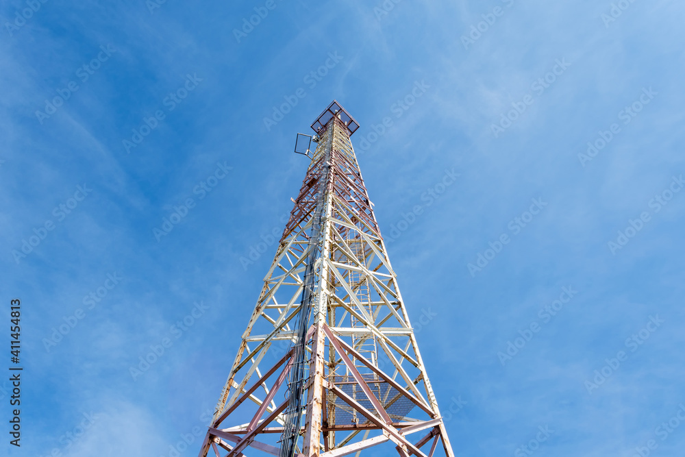 Metal tower for mobile communications, against the blue sky. Bottom view.
