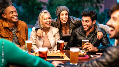 Happy friends drinking beer at brewery bar dehor - Friendship lifestyle concept with young milenial people enjoying time together at open air pub - Warm color tones on vivid filter with focus on girls photo