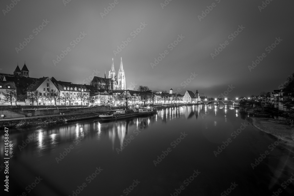 Fototapeta premium Blick zu der steinerne Brücke in Regensburg nachts im Nebel über den Fluss Donau mit dem beleuchteten Dom und historischer Altstadt , Deutschland