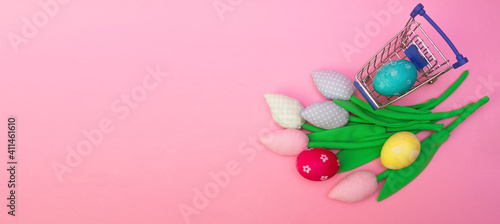 Painted easter eggs in shopping trolley and spring tulips flowers on pink background with copy space. Easter eco banner. shopping and zero waste.