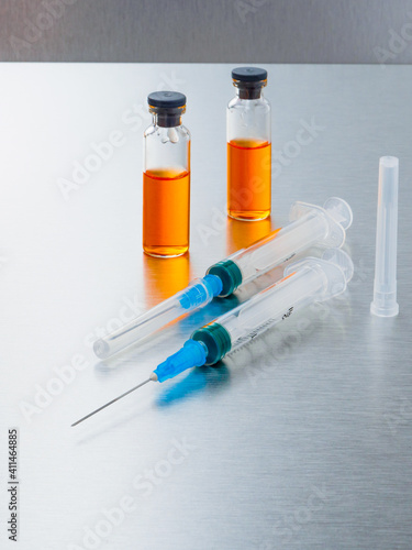 Selective focus. Syringes and ampoules with orange coronavirus vaccine on a silver aluminum background. Covid-19 pandemic medical concept. Copy space.