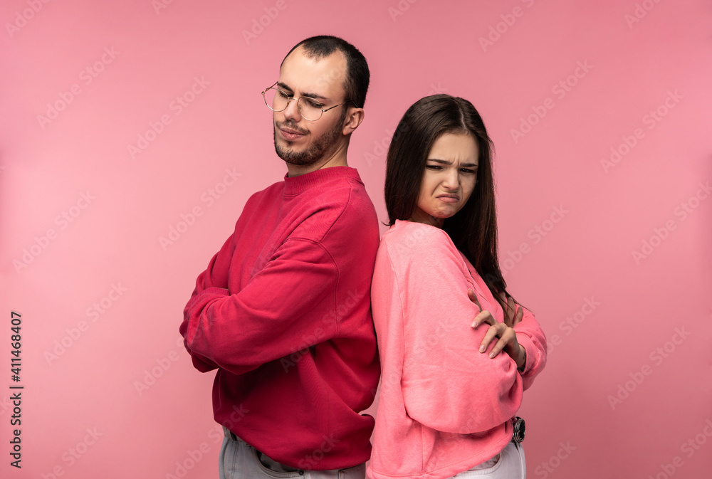 Fototapeta premium Photo of attractive couple stands back to back and looks resentful and desperate, isolated over pink background