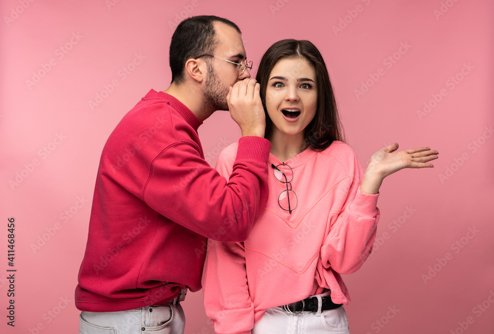 Photo of sweet couple, man whispers some secrets or sales to his girlfriend and she is surprised, isolated over pink background Photo of sweet couple, man whispers some secrets or sales to his girlfriend and she is surprised, isolated over pink background