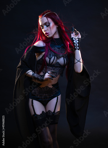 Redhead vampire woman posing on black background in lace lingerie and heels