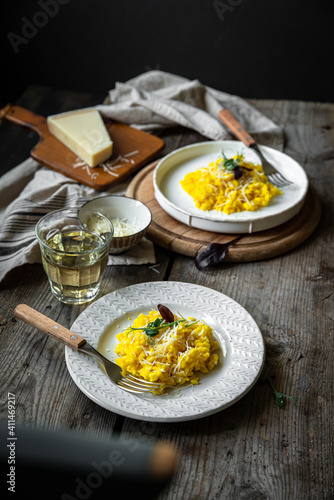 Rustic dinner for two with risotto all Milanese and wine. Risotto with Saffron and parmesan on white plate on wooden table. 