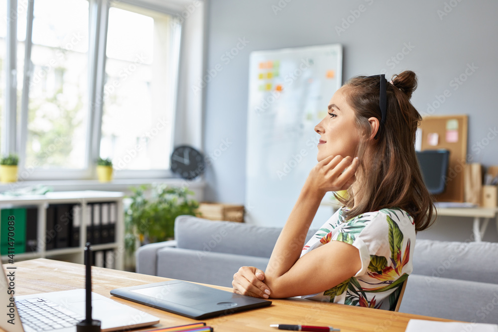 Thoughtful female graphic designer sitting at desk working from home office Thoughtful female graphic designer sitting at desk working from home office