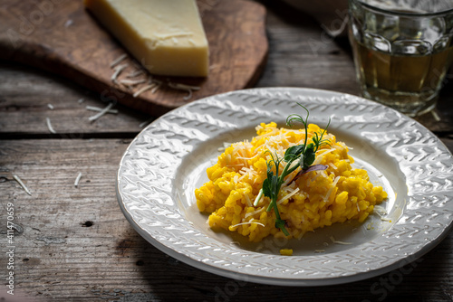 Rustic dinner with risotto all Milanese. Risotto with Saffron and parmesan on white plate on wooden table. 