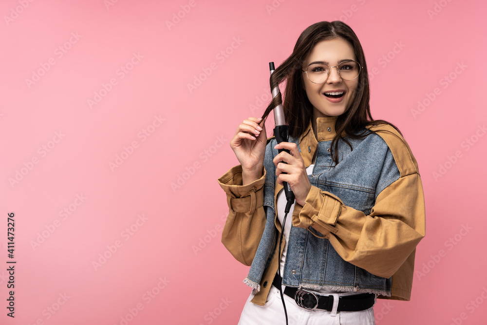 Photo of attractive lady holds curling hair, smile happy lucky purchase, wears casual jeans jacket white undershirt isolated pink color background Photo of attractive lady holds curling hair, smile happy lucky purchase, wears casual jeans jacket white undershirt isolated pink color background