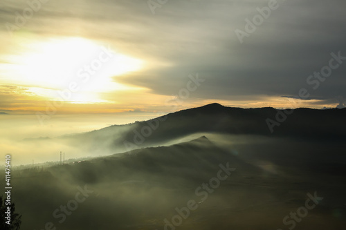 Misty valley at warm sunrise on a cloudy sky background
