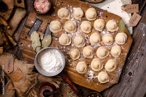 homemade dumplings with meat on rustic wooden board and table with flour, sackcloth