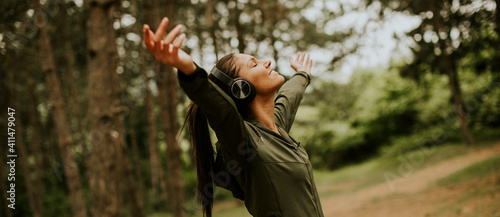 Young woman with earphones preading her arms in the forest because she enjoys training outside photo