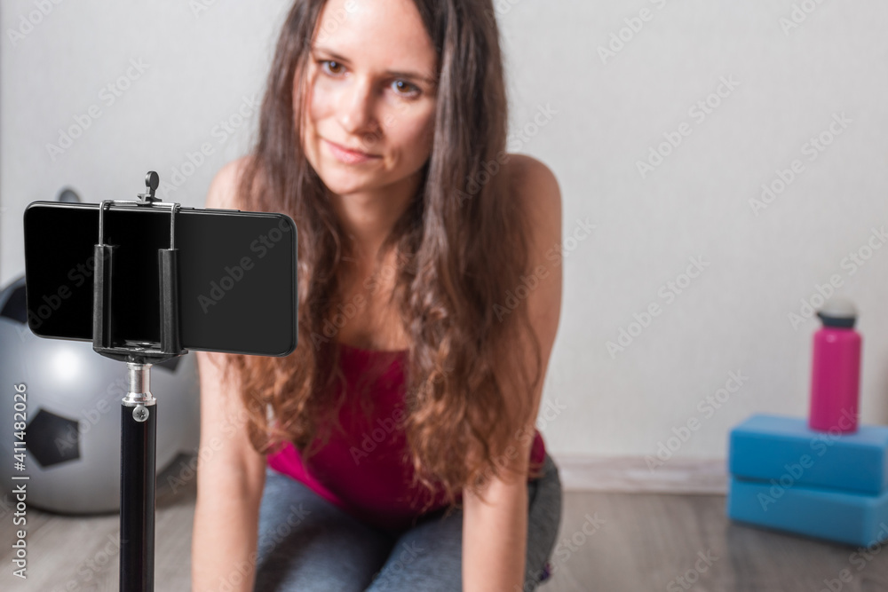 Fitnes young woman sitting on the floor and looking at mobile phone. Yoga blocks, fitball and water bottle are in the background. Close-up. Selective focus. Fitnes young woman sitting on the floor and looking at mobile phone. Yoga blocks, fitball and water bottle are in the background. Close-up. Selective focus.