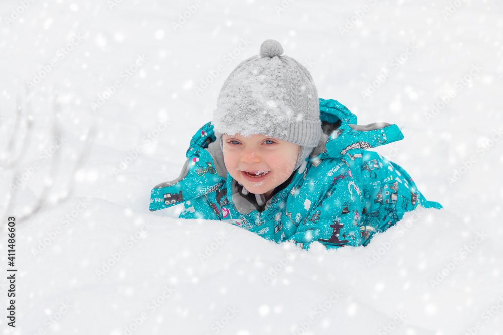 Cute little boy happily playing in the white fluffy fresh snow outdoors in winter. The child tries to take a snowball. Happy Childhood. Game Cute little boy happily playing in the white fluffy fresh snow outdoors in winter. The child tries to take a snowball. Happy Childhood. Game