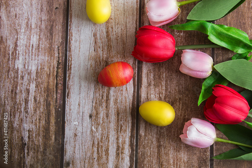 Pink and red tulips and Easter eggs on a brown wooden background. Spring background. Background for design. Easter. Copy space.
