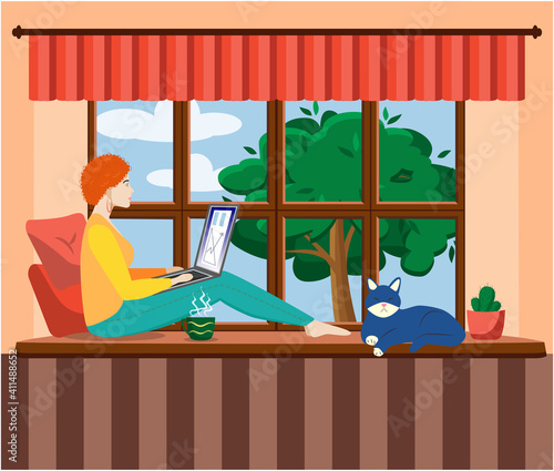 A woman works at a laptop while sitting on the windowsill at home. Freelance concept, quarantine due to covid-19.