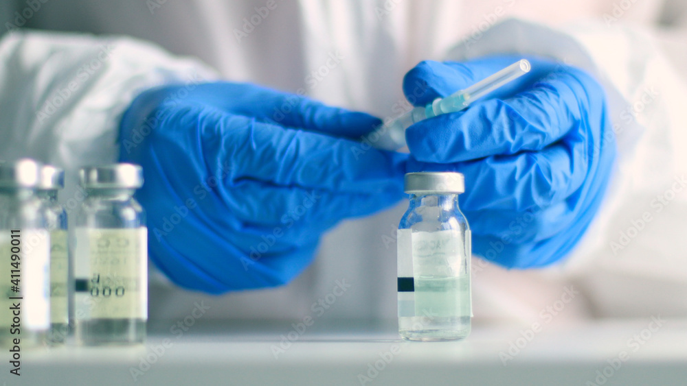 Fototapeta premium Nurse or doctor in medical protective uniform and latex rubber fill in syringe with medicine from glass vial while preparing for work during coronavirus, flu or measles pandemic for poster, web banner