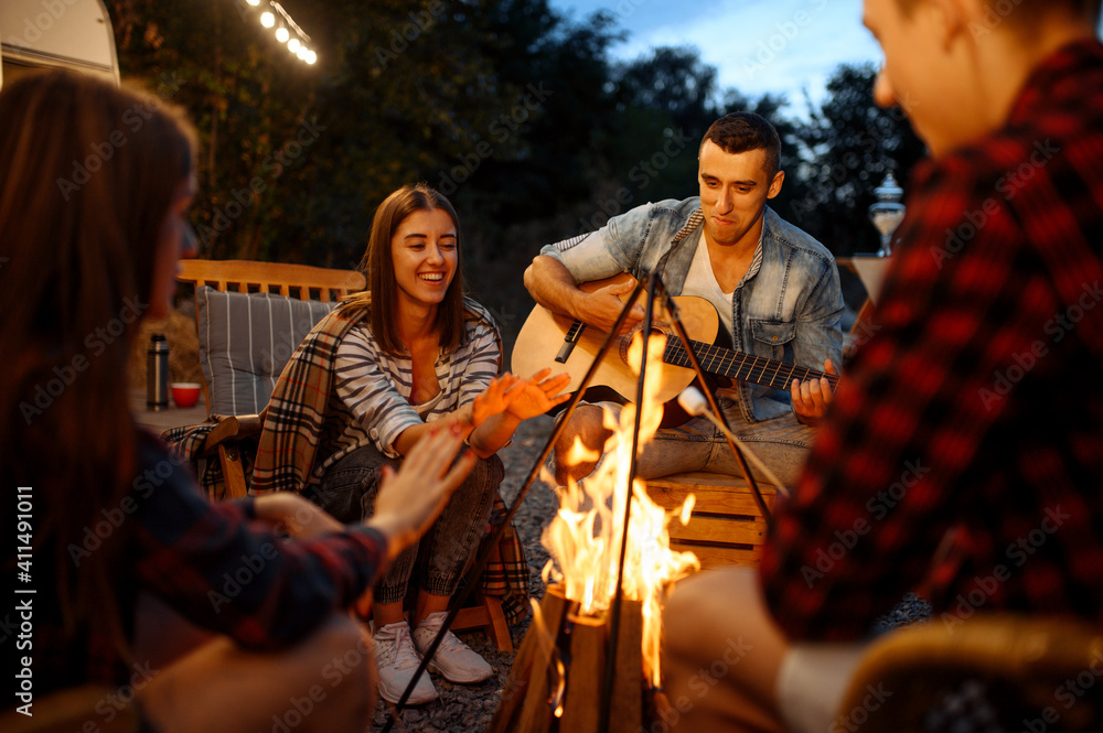 Friends playing on guitar by the bonfire, camping Friends playing on guitar by the bonfire, camping