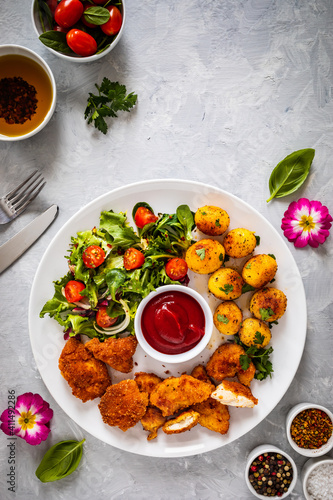 Fried breaded chicken nuggets with fried potatoes and fresh vegetables 
