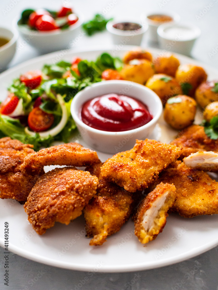 Fried breaded chicken nuggets with fried potatoes  and fresh vegetables
